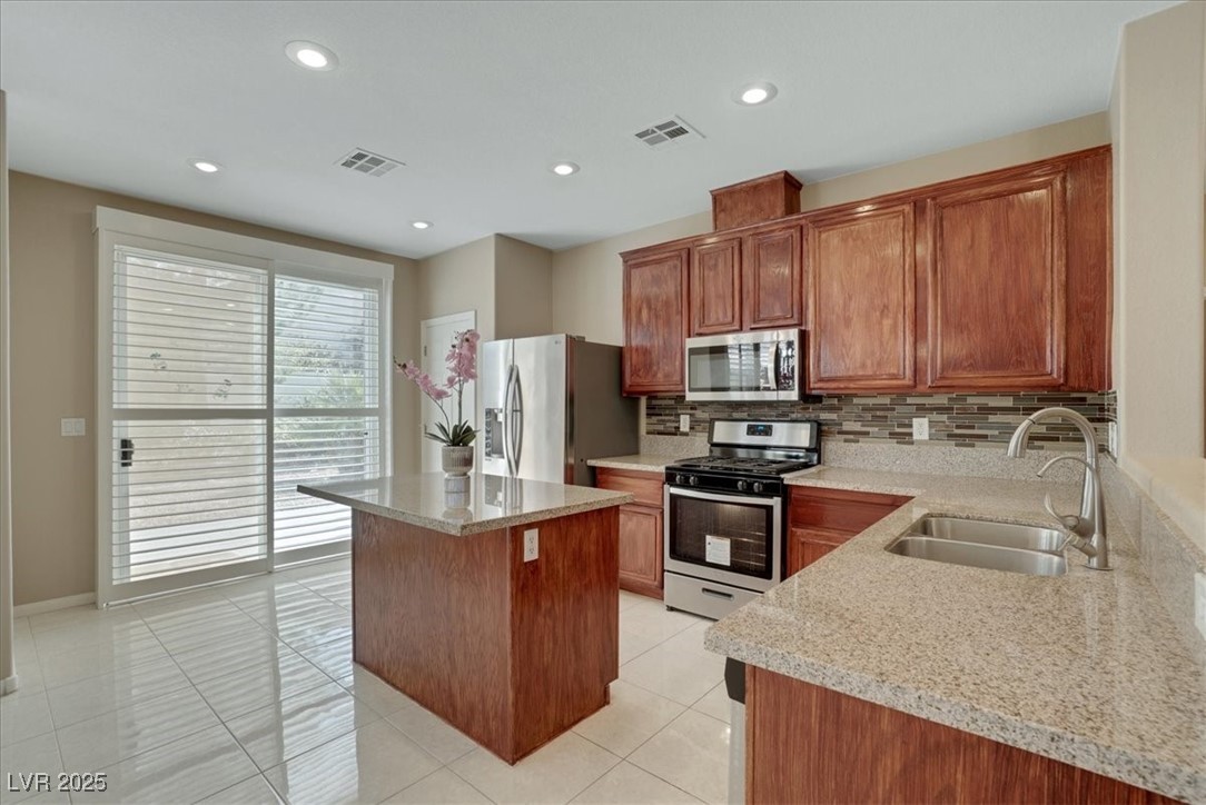319 Fox Lake Avenue Las Vegas, NV 89148 - Photo 22 of 39 Kitchen with stainless steel appliances, light stone counters, tasteful backsplash, light tile patterned floors, and a center island