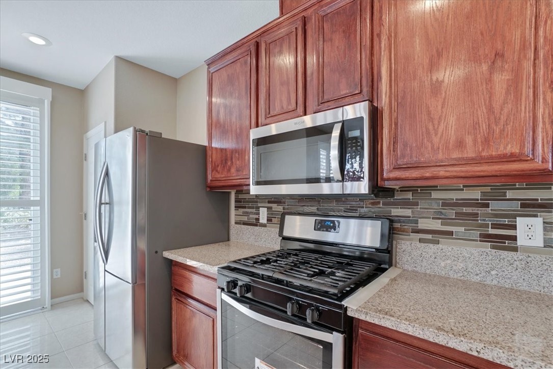 319 Fox Lake Avenue Las Vegas, NV 89148 - Photo 24 of 39 Kitchen featuring stainless steel appliances, backsplash, light stone countertops, and light tile patterned floors