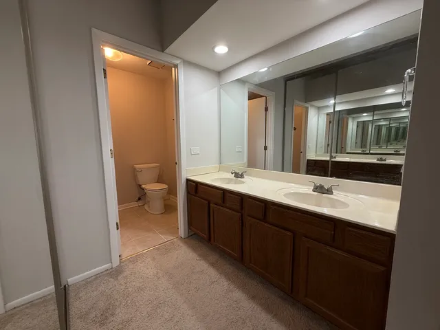 a bathroom with a double vanity sink and mirror with toilet