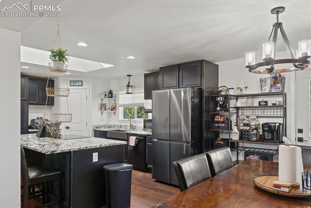 28079 Iris Road Pueblo, CO 81006 - Photo 18 of 50 Kitchen featuring black dishwasher, hanging light fixtures, light stone countertops, stainless steel refrigerator, and dark hardwood / wood-style floors