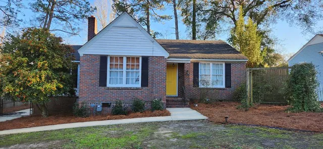 a view of a brick house with a yard plants and large tree
