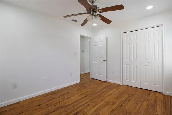 an empty room with wooden floor fan and windows