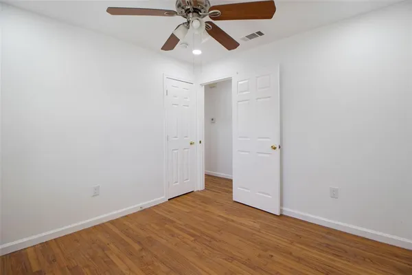 an empty room with wooden floor ceiling fan and windows