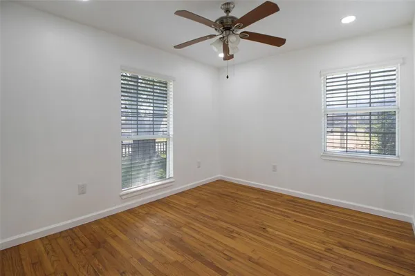 an empty room with wooden floor fan and windows