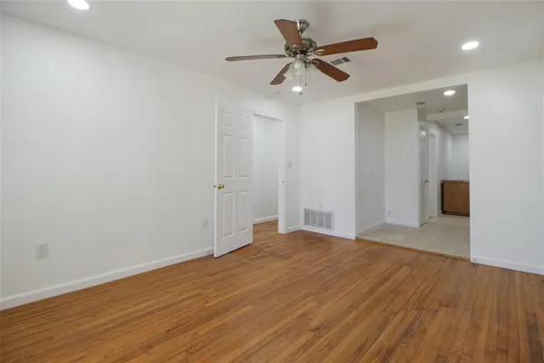 a view of an empty room with wooden floor and a ceiling fan