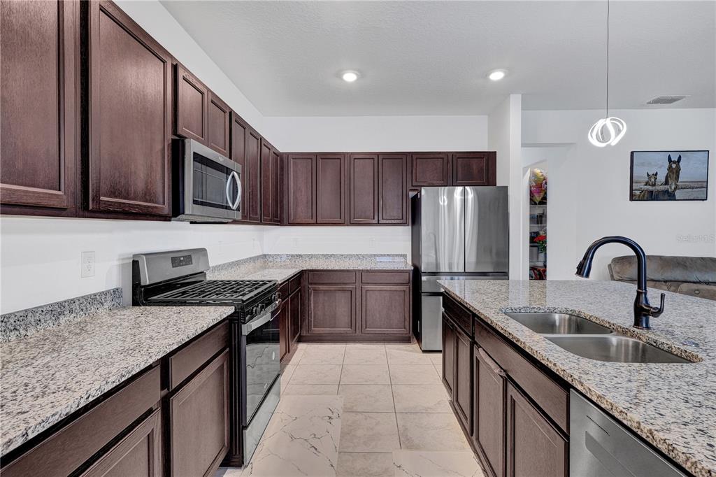 7185 Southwest 63rd Street Ocala, FL 34474 - Photo 13 of 31 a kitchen with granite countertop stainless steel appliances a sink dishwasher a refrigerator a stove top oven a sink and dishwasher