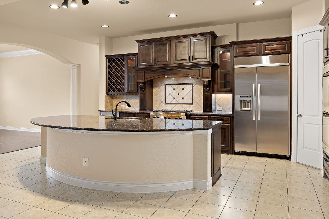 174 Estrella Crossing Georgetown, TX 78628 - Photo 11 of 39 Kitchen featuring glass insert cabinets, dark brown cabinetry, dark stone countertops, arched walkways, and stainless steel built in refrigerator