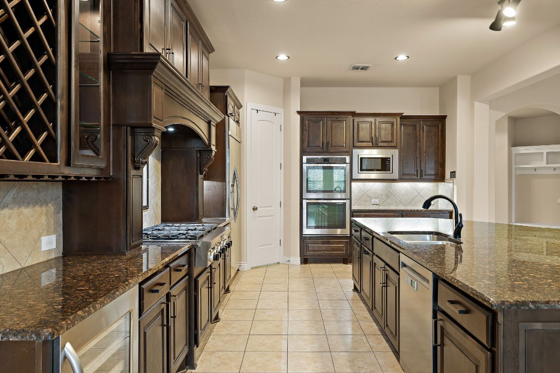 174 Estrella Crossing Georgetown, TX 78628 - Photo 14 of 39 Kitchen with dark brown cabinetry, beverage cooler, dark stone counters, appliances with stainless steel finishes, and recessed lighting