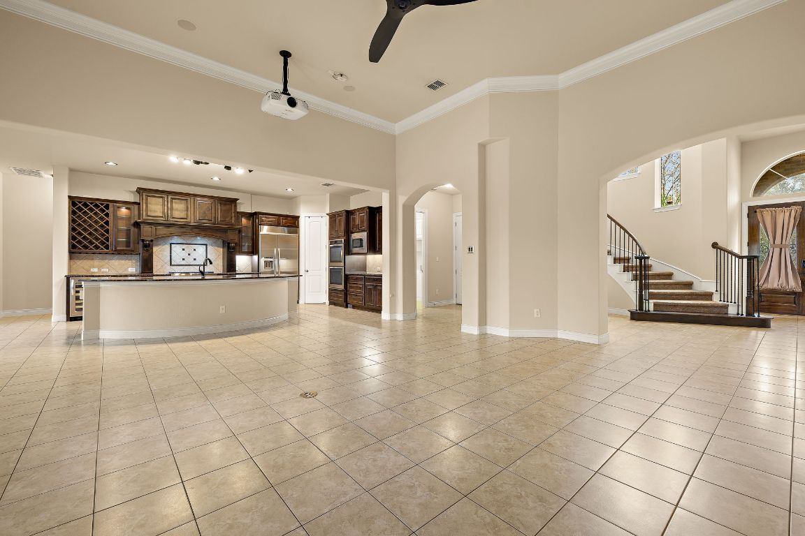 174 Estrella Crossing Georgetown, TX 78628 - Photo 7 of 39 Unfurnished living room featuring crown molding, stairs, light tile patterned floors, ceiling fan, and arched walkways