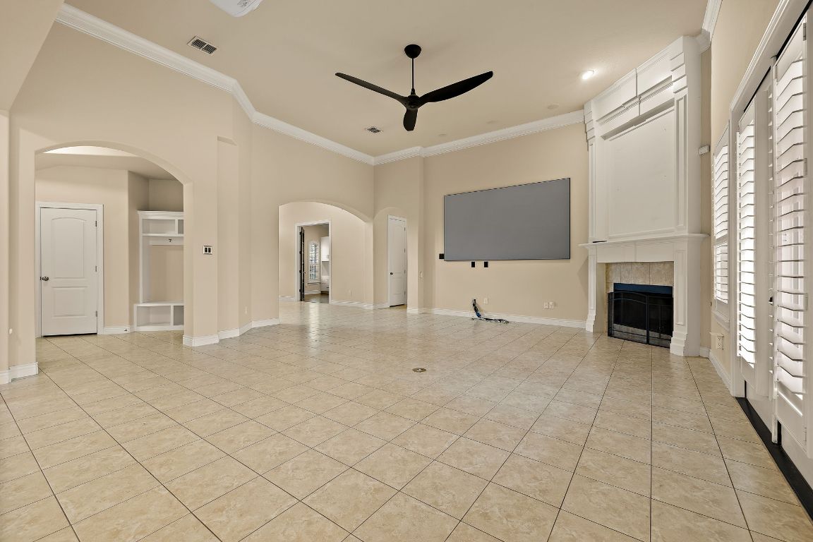 174 Estrella Crossing Georgetown, TX 78628 - Photo 10 of 39 Unfurnished living room with a tiled fireplace, crown molding, arched walkways, ceiling fan, and light tile patterned floors