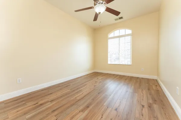 an empty room with wooden floor chandelier fan and windows
