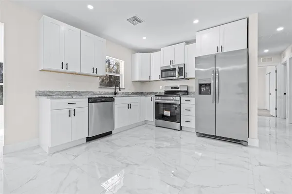 a kitchen with stainless steel appliances granite countertop a stove top oven a refrigerator and white cabinets