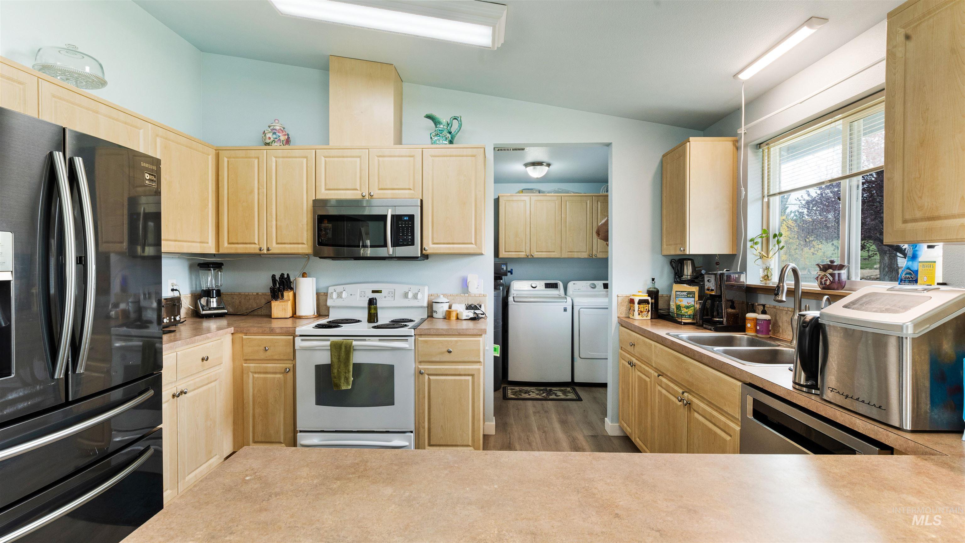 731 Tower Lane Caldwell, ID 83607 - Photo 26 of 38 Kitchen with stainless steel appliances, light wood finish cabinetry, washer and clothes dryer, vaulted ceiling, and light countertops