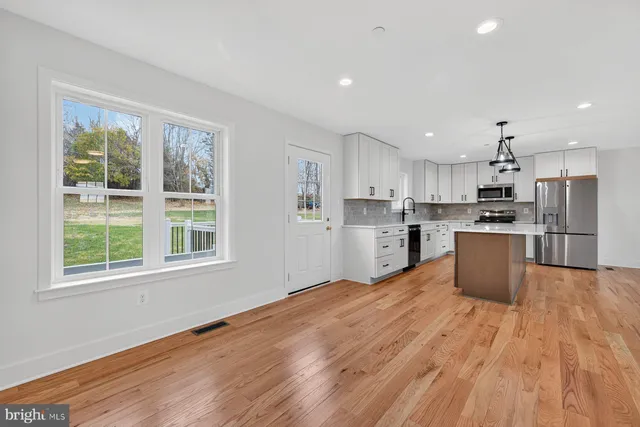 a kitchen with stainless steel appliances kitchen island wooden floors wooden cabinets and a refrigerator