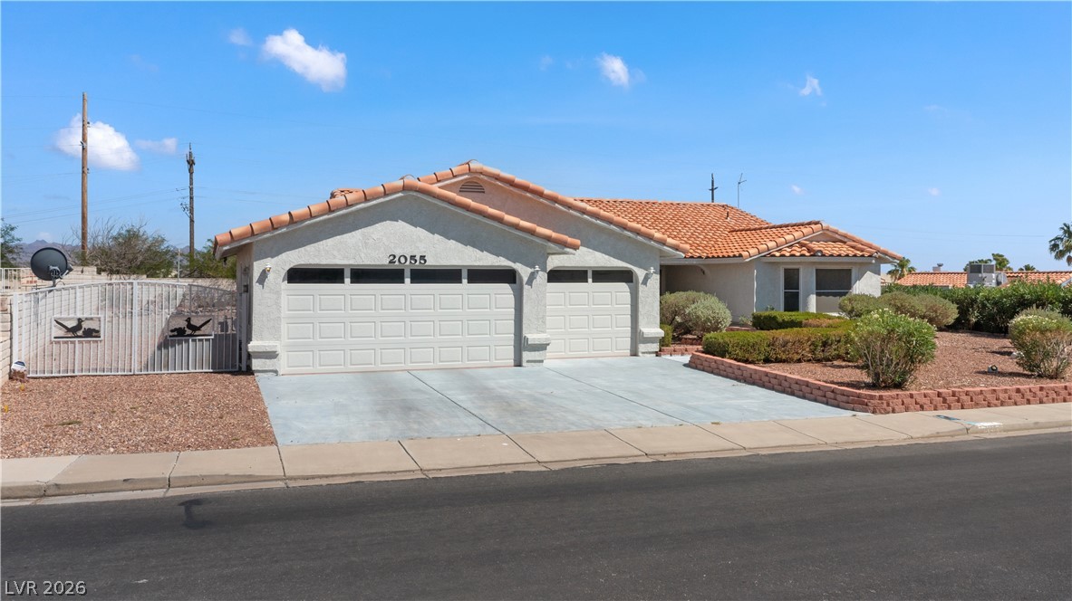 2055 Cholla Way Laughlin, NV 89029 - Photo 65 of 87 A well-maintained stucco home with a double garage and terracotta roof tiles, complemented by neat, desert-friendly landscaping.