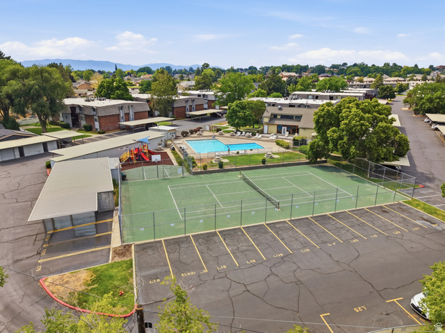 1700 Hickory Lane Provo, UT 84604 - Photo 3 of 20 Outdoor tennis court with chain-link fencing, adjacent to a swimming pool, covered parking structures, residential buildings, and a visible playground area
