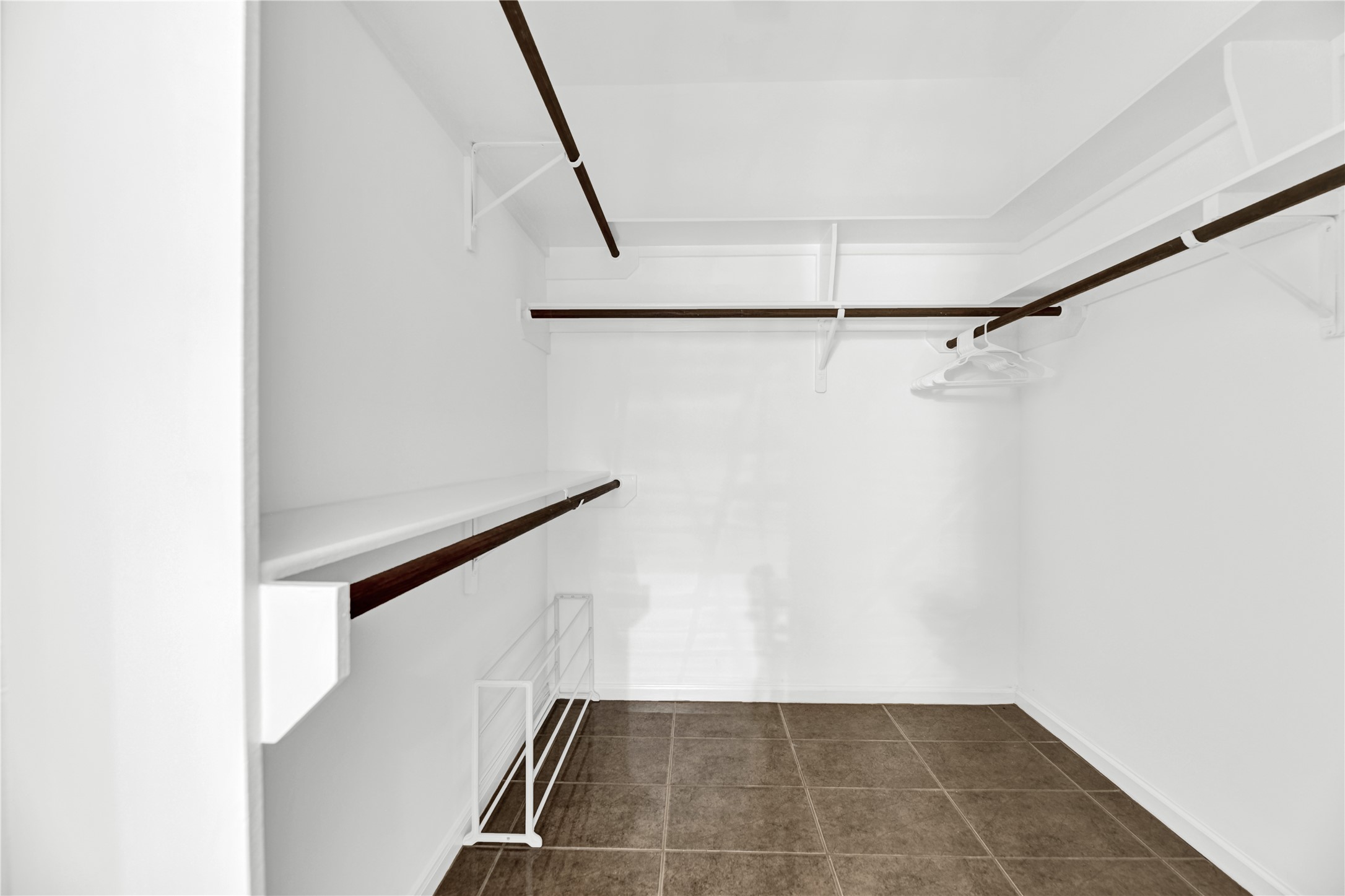 14420 Walters Road, Unit 16 Houston, TX 77014 - Photo 16 of 27 This photo shows a spacious walk-in closet with tiled flooring, white walls, and multiple dark wooden hanging rods and shelves for ample storage.
