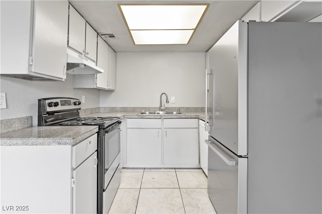 Kitchen featuring appliances with stainless steel finishes, light countertops, white cabinets, under cabinet range hood, and light tile patterned flooring
