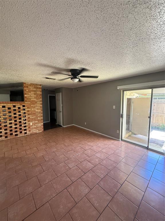 708 East Pecan Street, Unit 712 Hurst, TX 76053 - Photo 4 of 15 Spacious room featuring terra cotta tile flooring, a brick accent wall, and a ceiling fan with integrated lighting