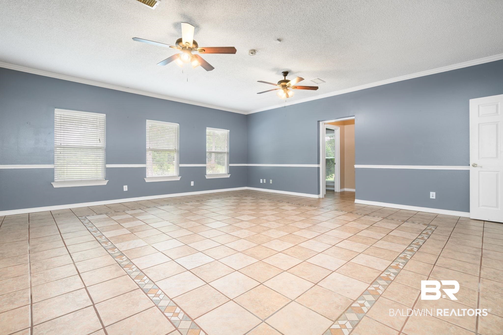 7540 2 Mile Road Irvington, AL 36544 - Photo 32 of 82 Expansive interior room featuring light-toned tile flooring with a decorative border, two ceiling fans, and multiple windows with blinds