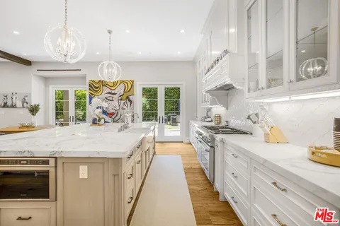 a large kitchen with stainless steel appliances kitchen island granite countertop a large stove a sink dishwasher and white cabinets with wooden floor