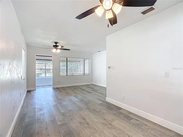 an empty room with wooden floor chandelier fan and windows