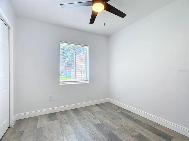 an empty room with wooden floor ceiling fan and window