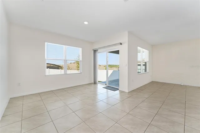 an empty room with windows and way to kitchen