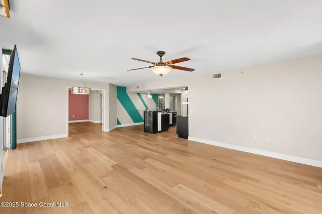 a view of an empty room with wooden floor and a ceiling fan