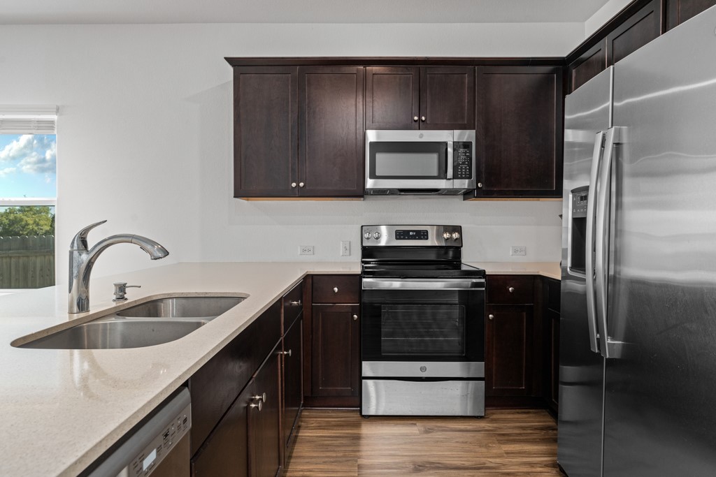 205 Rooster Way Jarrell, TX 76537 - Photo 3 of 29 Kitchen featuring appliances with stainless steel finishes, dark wood-style floors, dark brown cabinets, and light stone counters