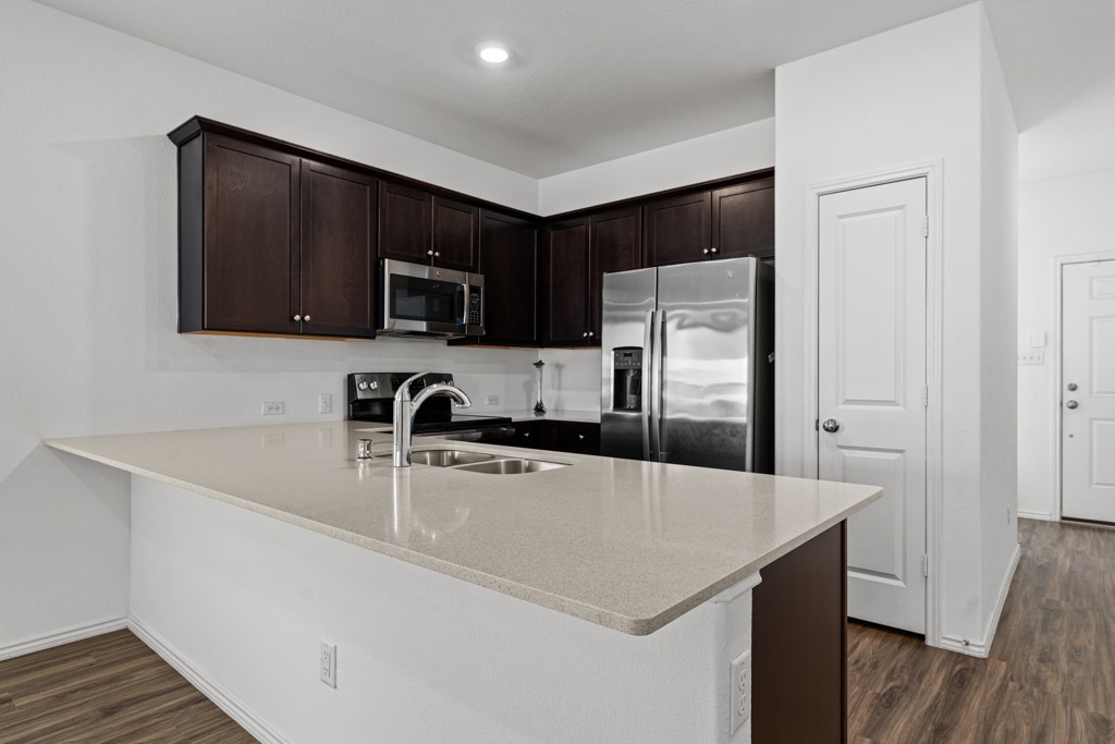 205 Rooster Way Jarrell, TX 76537 - Photo 4 of 29 Kitchen with stainless steel appliances, dark brown cabinets, dark wood finished floors, a peninsula, and light stone counters