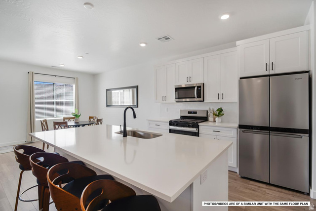 1702 Ripple Rock Drive, Unit 3171 Washington, UT 84780 - Photo 2 of 16 Modern kitchen featuring a large island with a stainless steel sink, white cabinetry, and stainless steel appliances