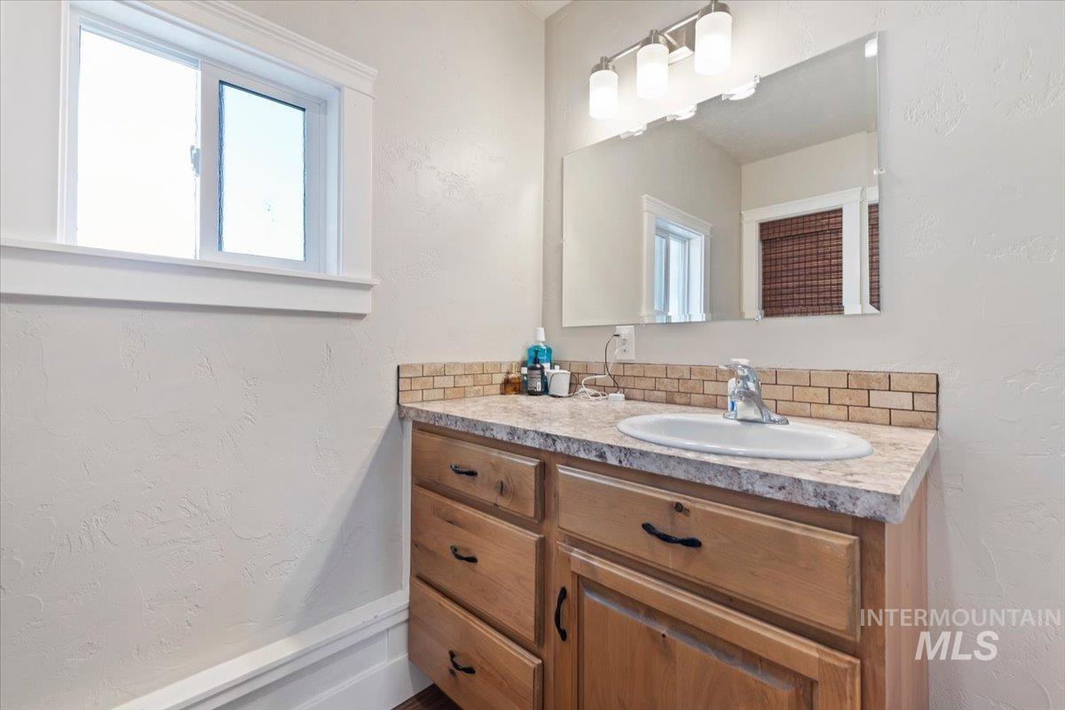 24240 Tiger Lane Caldwell, ID 83607 - Photo 45 of 50 Wood-finish vanity with an integrated sink, laminate countertop, tiled backsplash, and an overhead light fixture
