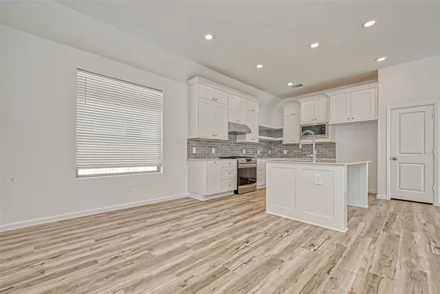 a kitchen with wooden floors white cabinets appliances