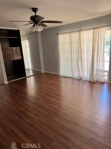 an empty room with wooden floor fan and windows