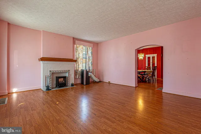 a view of an empty room with wooden floor fireplace and a window