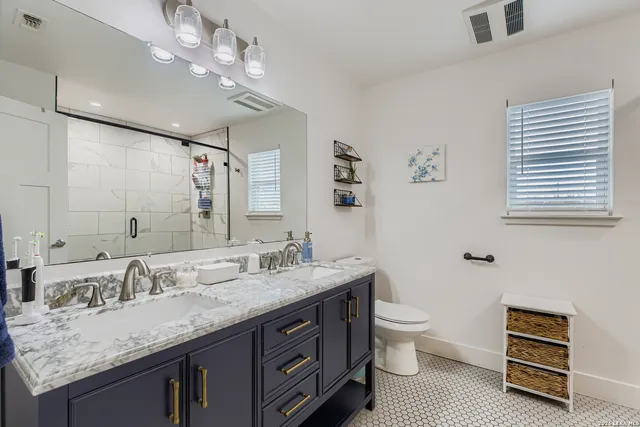 a bathroom with a granite countertop double vanity sink a toilet and a mirror