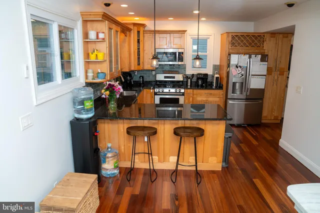 a kitchen with stainless steel appliances kitchen island granite countertop a refrigerator a stove a sink and white cabinets with wooden floor