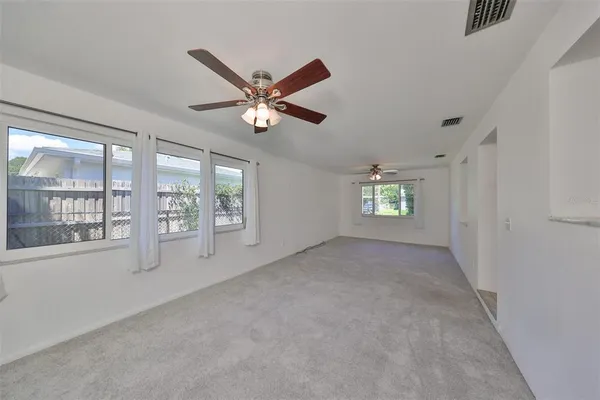an empty room with chandelier fan and windows