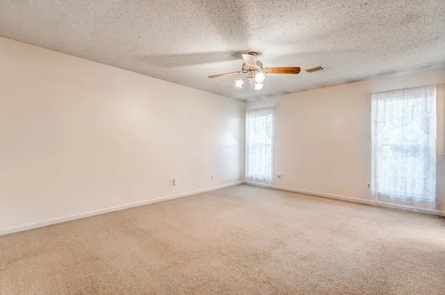 an empty room with chandelier fan and windows