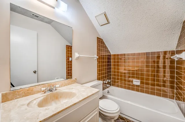 a bathroom with a granite countertop bathtub shower sink vanity mirror and toilet