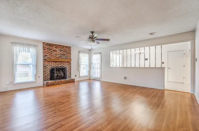 an empty room with wooden floor fireplace and windows