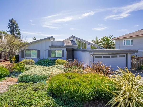 a front view of a house with lots of flower plants and wooden fence
