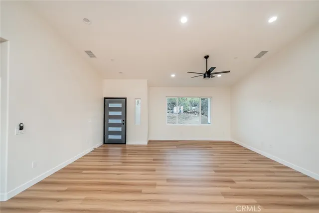 an empty room with wooden floor chandelier fan and windows