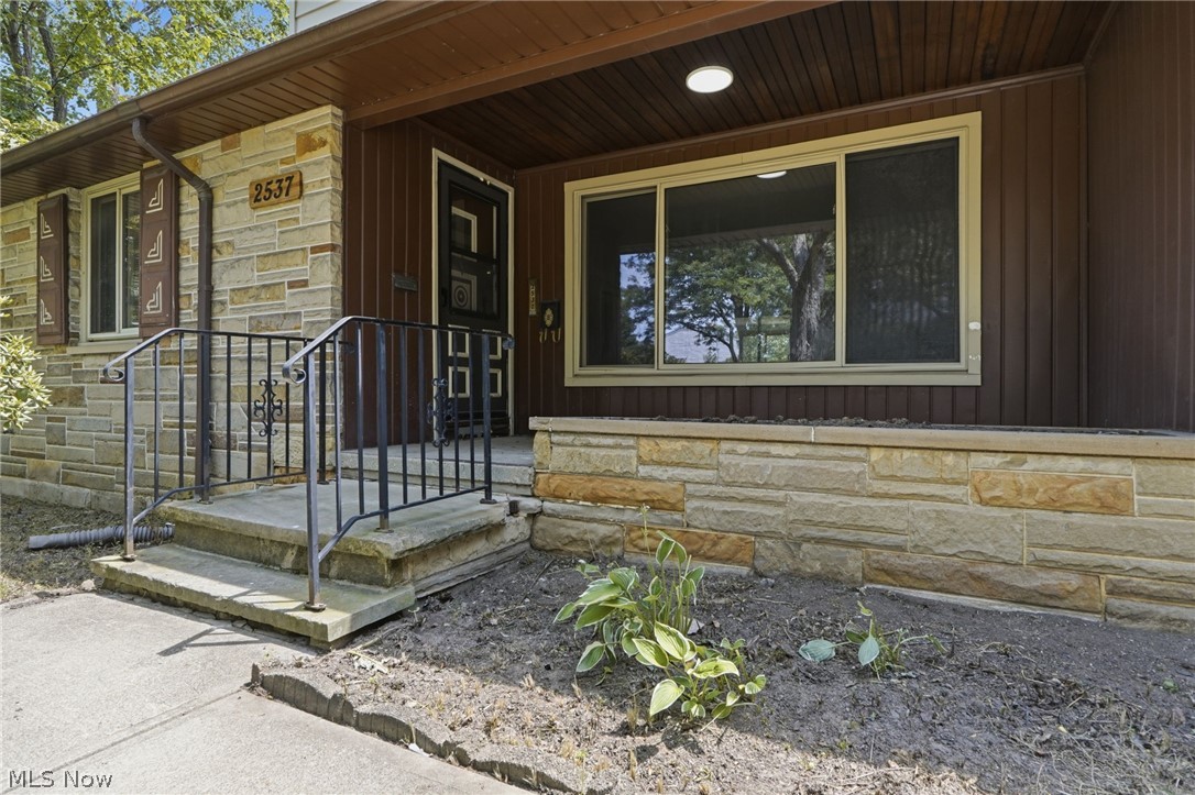 2537 Edgewood Road Beachwood, OH 44122 - Photo 2 of 39 Stone veneer facade featuring a front entrance with wrought iron railings, a covered patio, and board-and-batten siding accents