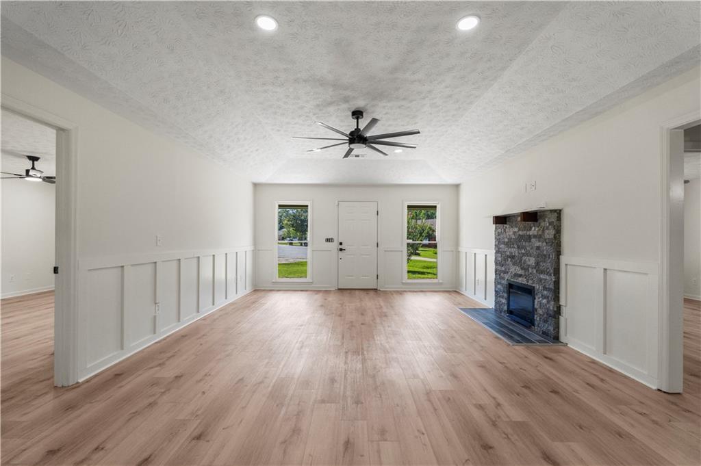 766 Lee Road Phenix City, AL 36870 - Photo 5 of 30 Unfurnished living room with ceiling fan, a stone fireplace, light wood-type flooring, a decorative wall, and a wainscoted wall
