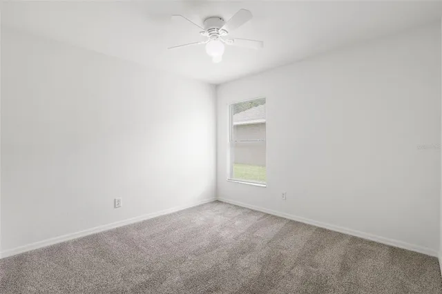 an empty room with a chandelier fan and windows