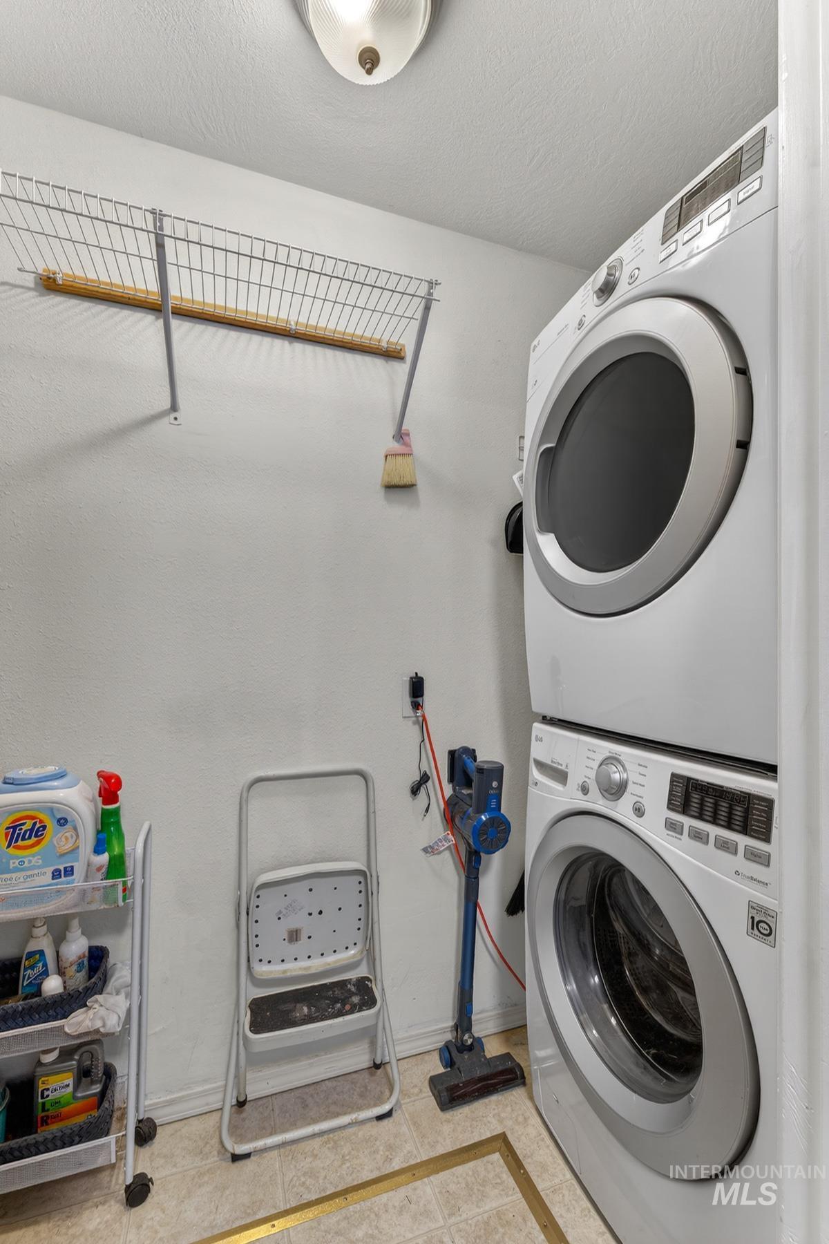 1801 Carico Road McCall, ID 83638 - Photo 21 of 30 Laundry room featuring stacked washer and clothes dryer, a textured ceiling, light tile patterned floors, and inlaid floor details