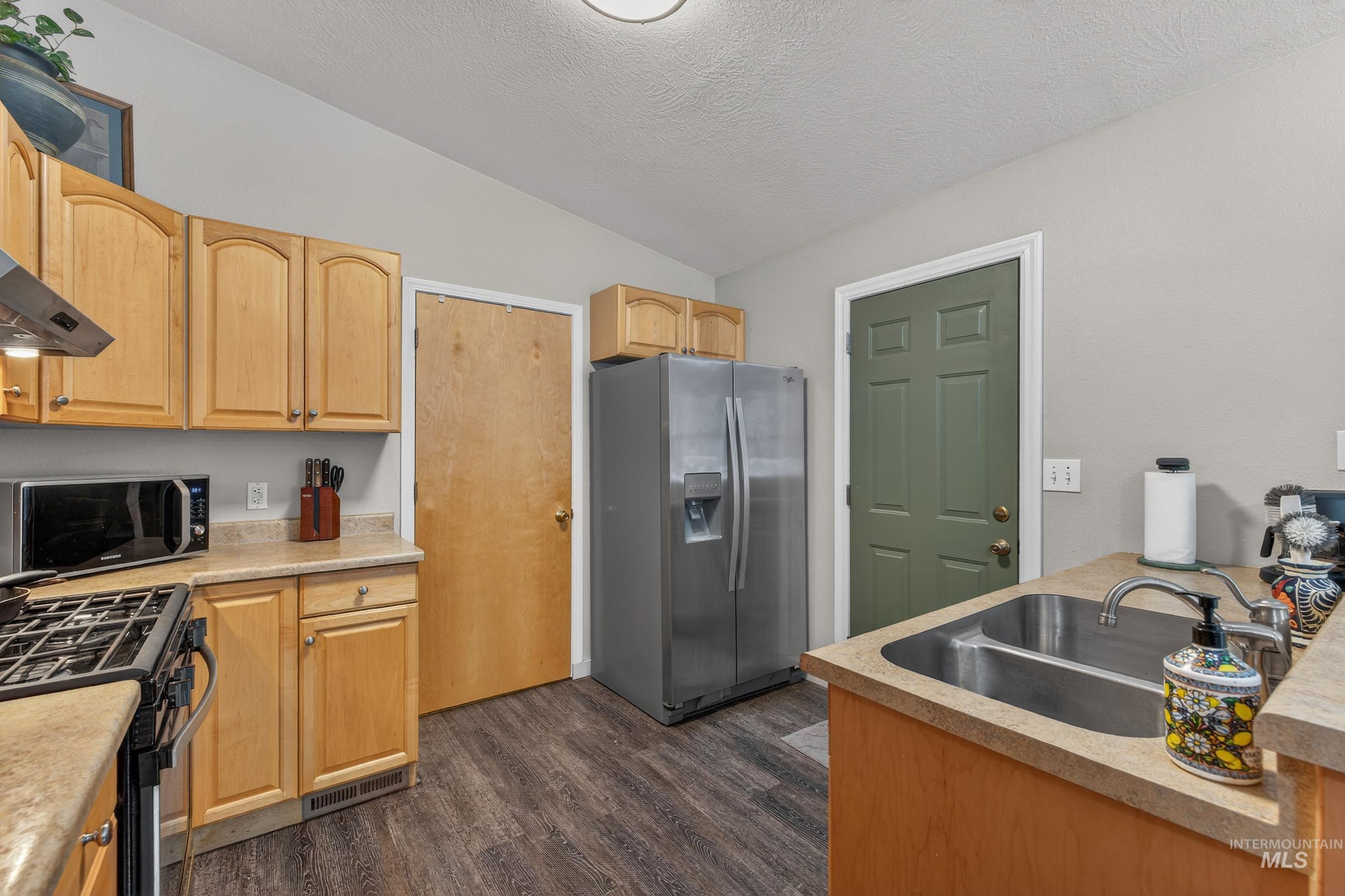 1801 Carico Road McCall, ID 83638 - Photo 26 of 30 Kitchen with stainless steel refrigerator with ice dispenser, light countertops, dark wood-style floors, black range with gas stovetop, and light wood finish cabinets