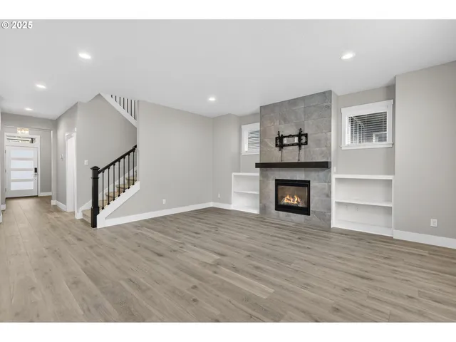 a view of an empty room with wooden floor fireplace and a window